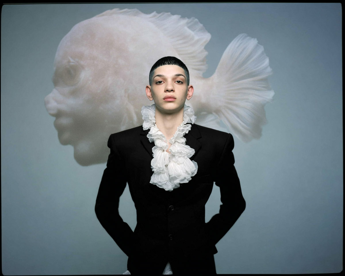 Portrait conceptuel d’un jeune créatif androgyne en veste noire, éclairage froid, projection d’une forme translucide évoquant la fusion de l’humain et de l’intelligence artificielle.